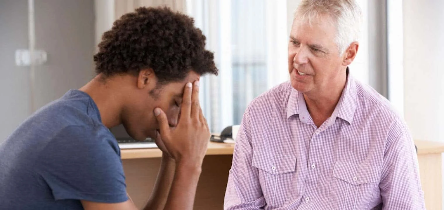 stress-and-drug-abuse Young man holds head while older man takes notes on notepad