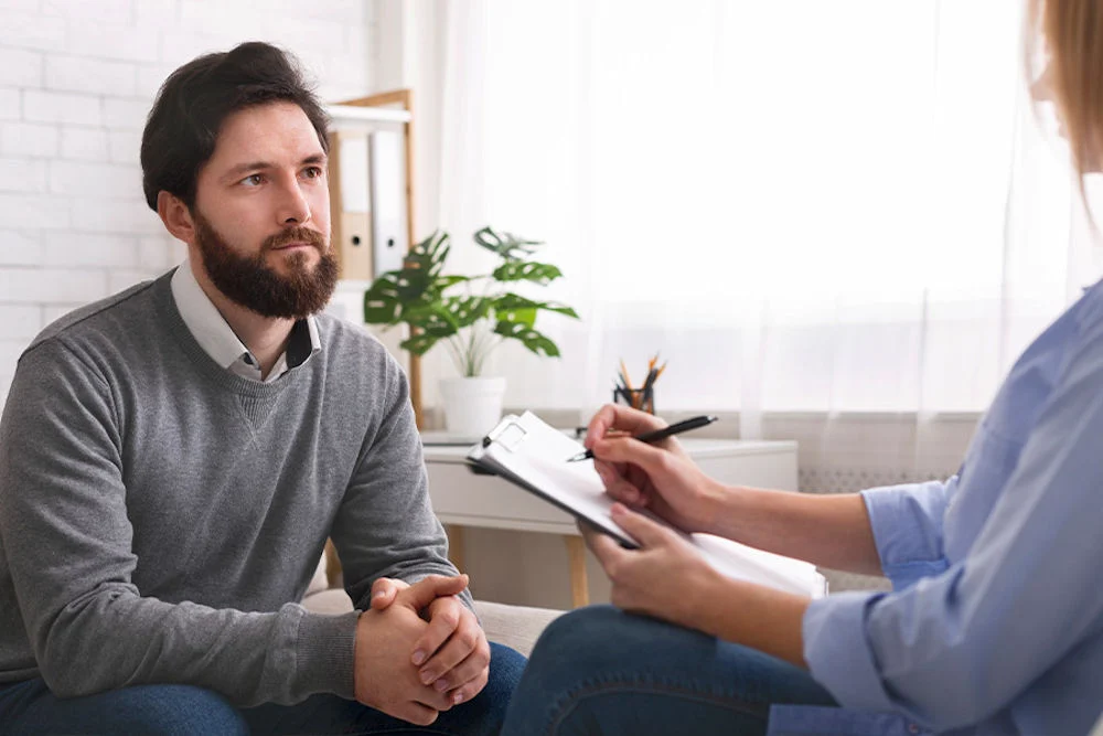 Young man in layered sweater sitting and listening to therapist running through list Young man in layered sweater sitting and listening to therapist running through list