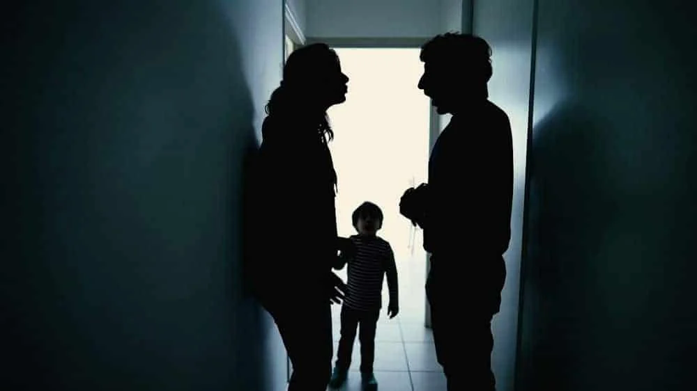 parents-addiction Shaded view of man and woman fighting in hallway while small boy watches