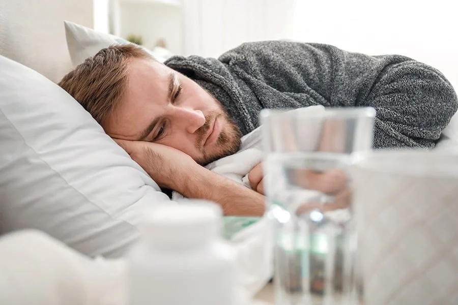 caffeine-withdrawal-recovery-timeline Man laying down in padded bed with water while undergoing caffeine detox