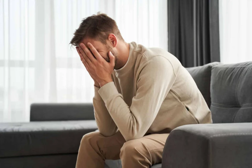 Man leaning forward and holding face in tiredness while sitting in couch.