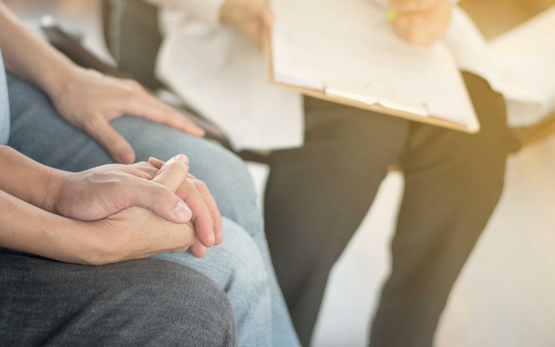 Couple holding hands while seated while addiction therapist takes notes on clipboard