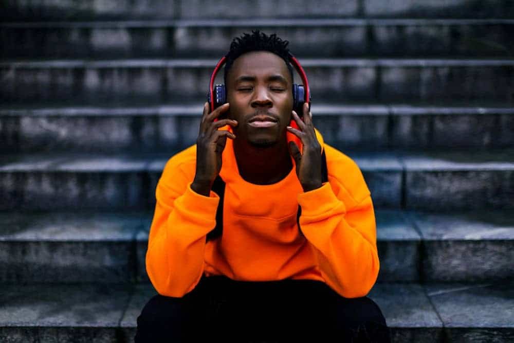 Man in bright orange hoodie listening to calm music through headphones with closed eyes