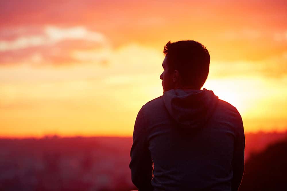 Man in hoodie contemplates in front of sunset