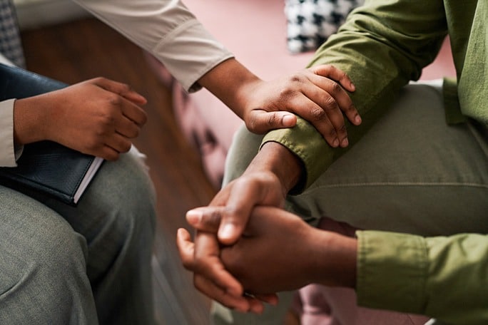 Picture of a seated therapist reassuring a client by holding their arm, pictured below the neck