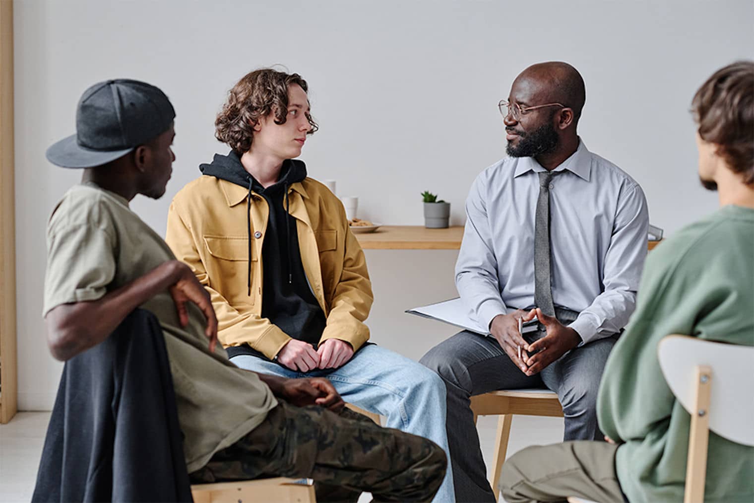 Therapist with clipboard talks to skeptical young men in addiction recovery group