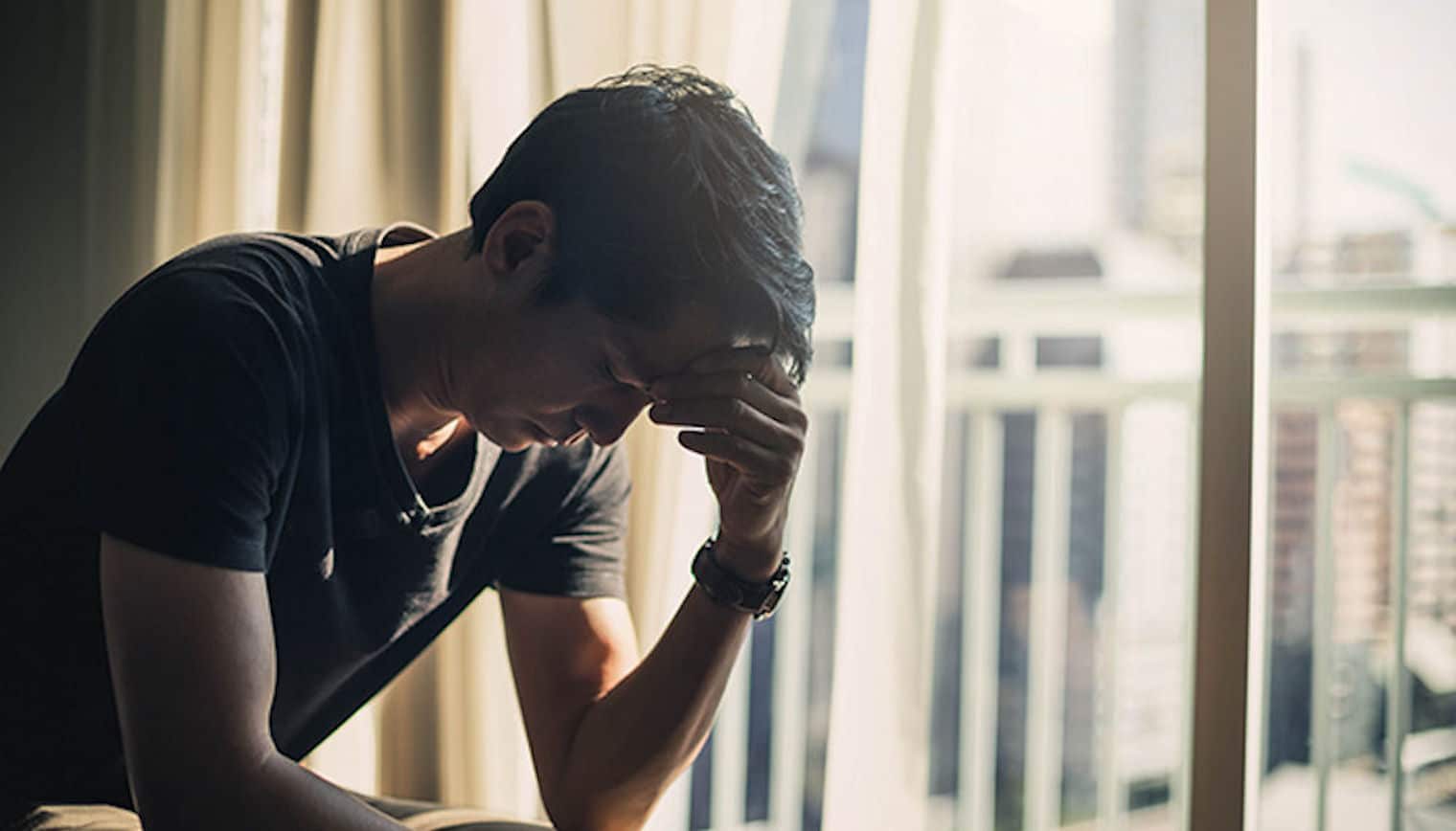 Young man holding head while sitting on a bed in an addiction recovery center