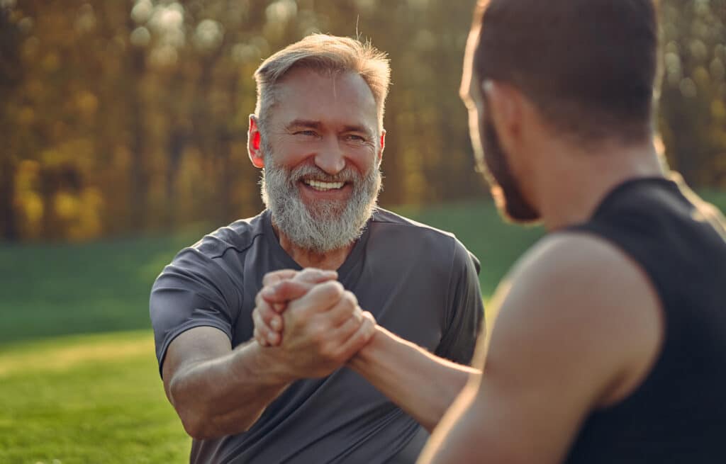 Older man and younger man clasping hands in helping friend with alcohol addiction