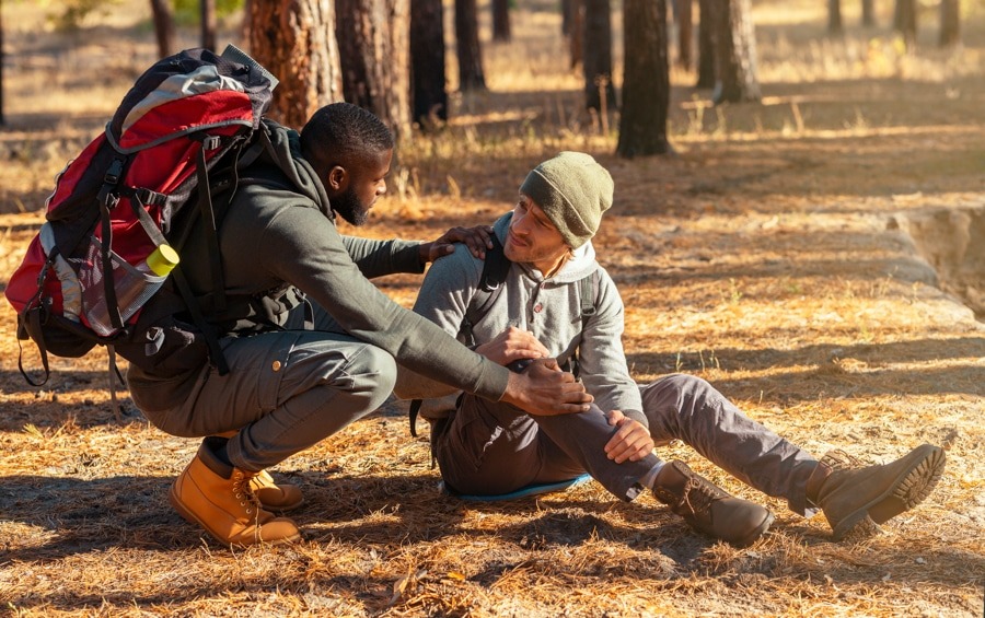 Man squatting to brace shin of fallen man in pain