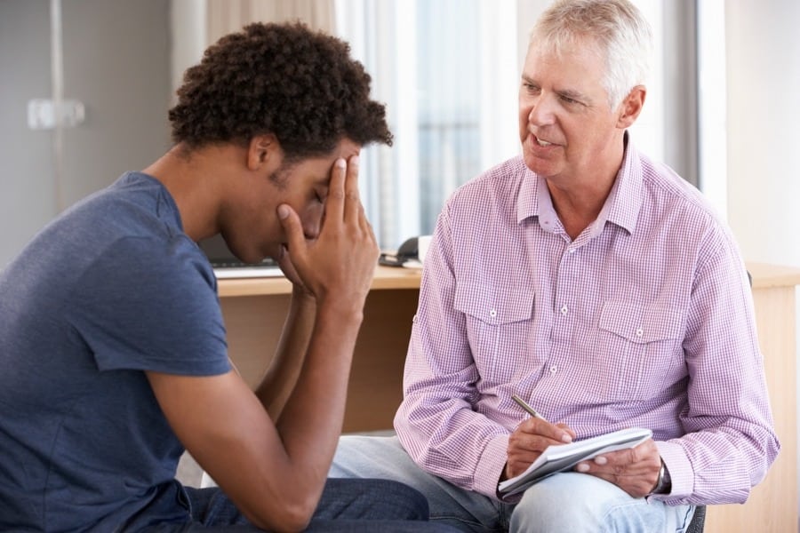 Man holding his head in frustration while discussing friend with alcoholism with older man