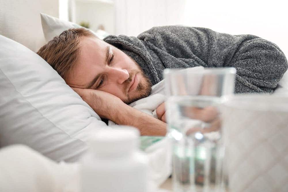 sad man laying in bed with cup of water on night stand