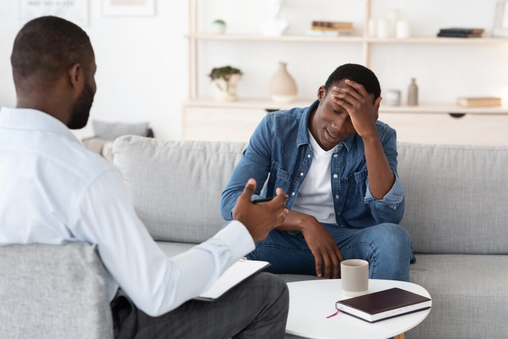 Young man rubs forehead while talking about stress with therapist