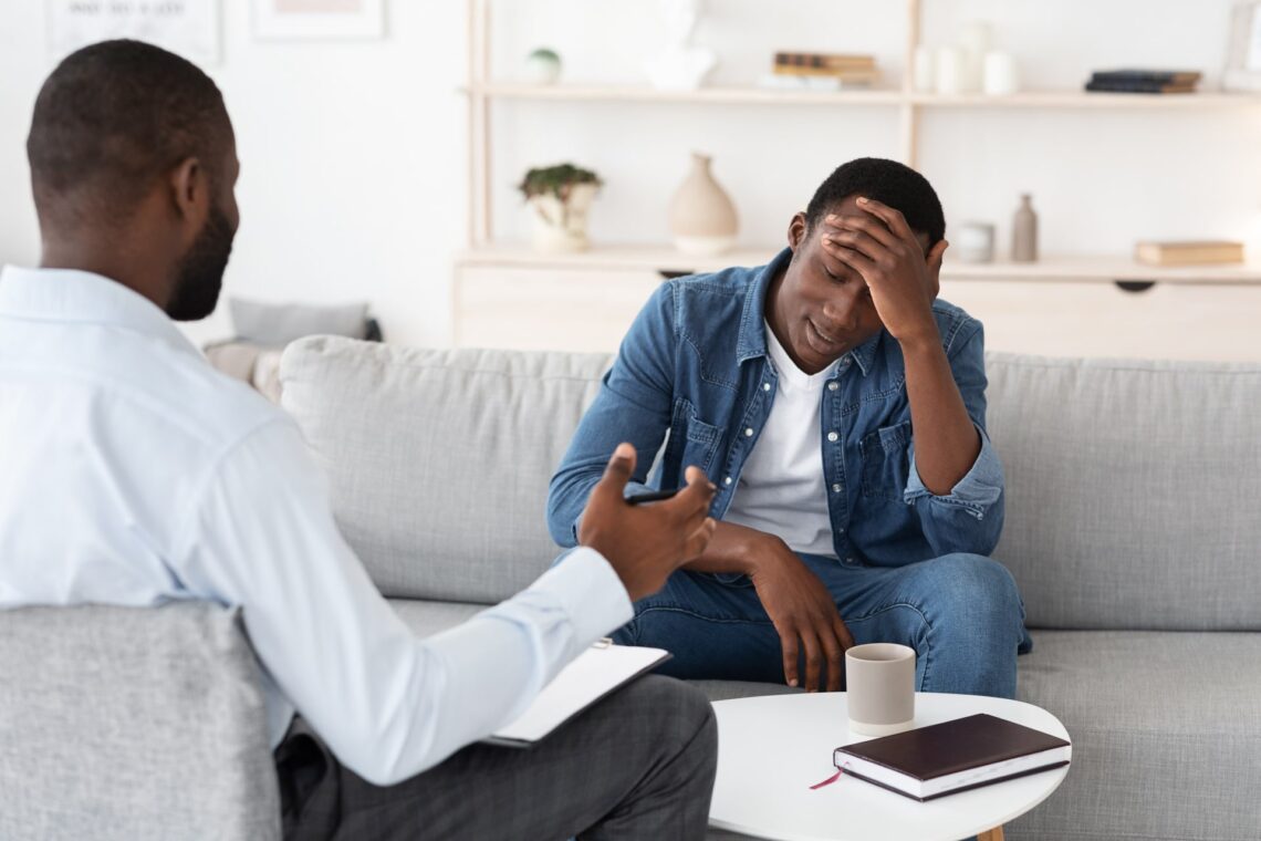 Young man rubs forehead while talking about stress with therapist