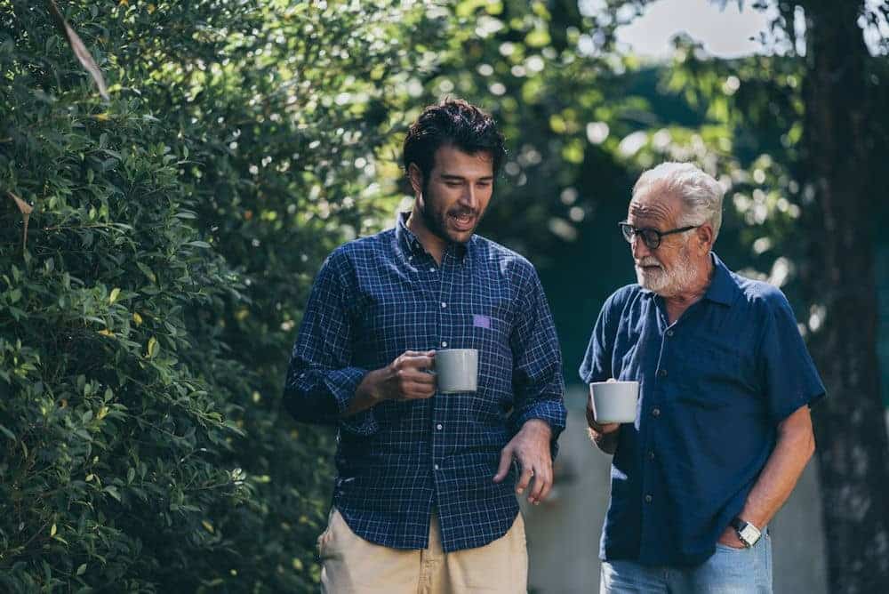 Younger man and older man sipping coffee from white mugs and discussing binge drinking