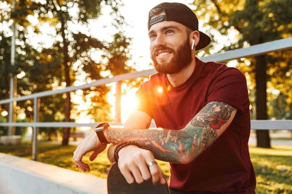 Man with tattoo sleeves listening to music on AirPods while sitting in bleachers