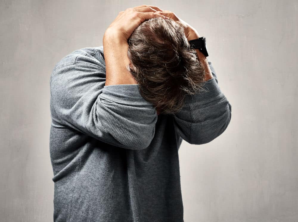 Anxious man wrapping arms over bent head.