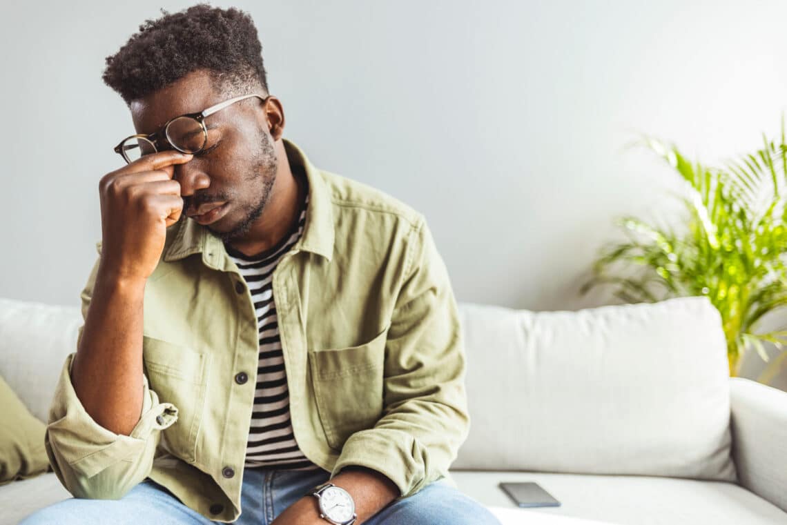 Man with PTSD reaching underneath glasses to pinch nose in frustration.