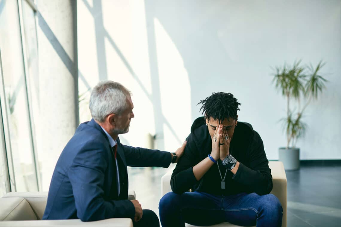 Older man comforting younger man as he describes body image issues.