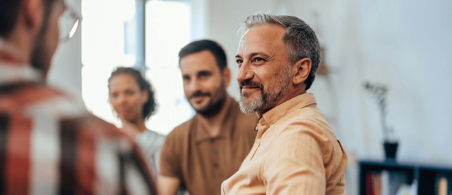 Older man sits through cocaine addiction support group with amused smile.