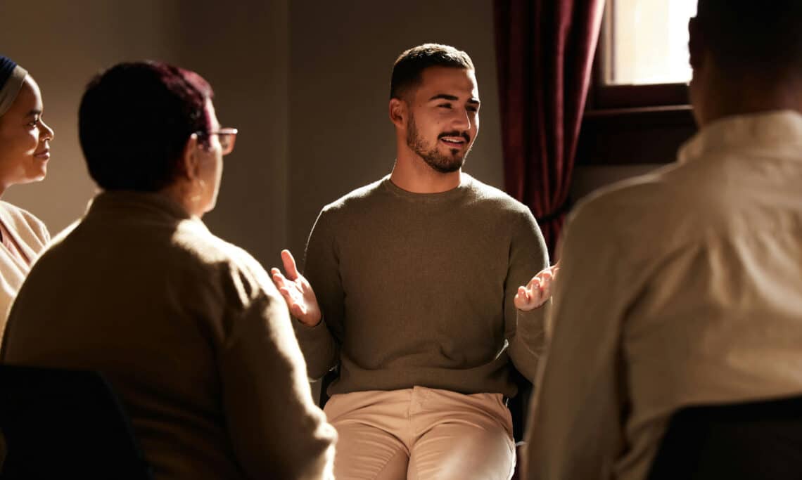 Man in shaded treatment room conversing with men and nonbinary people about binge eating disorder.