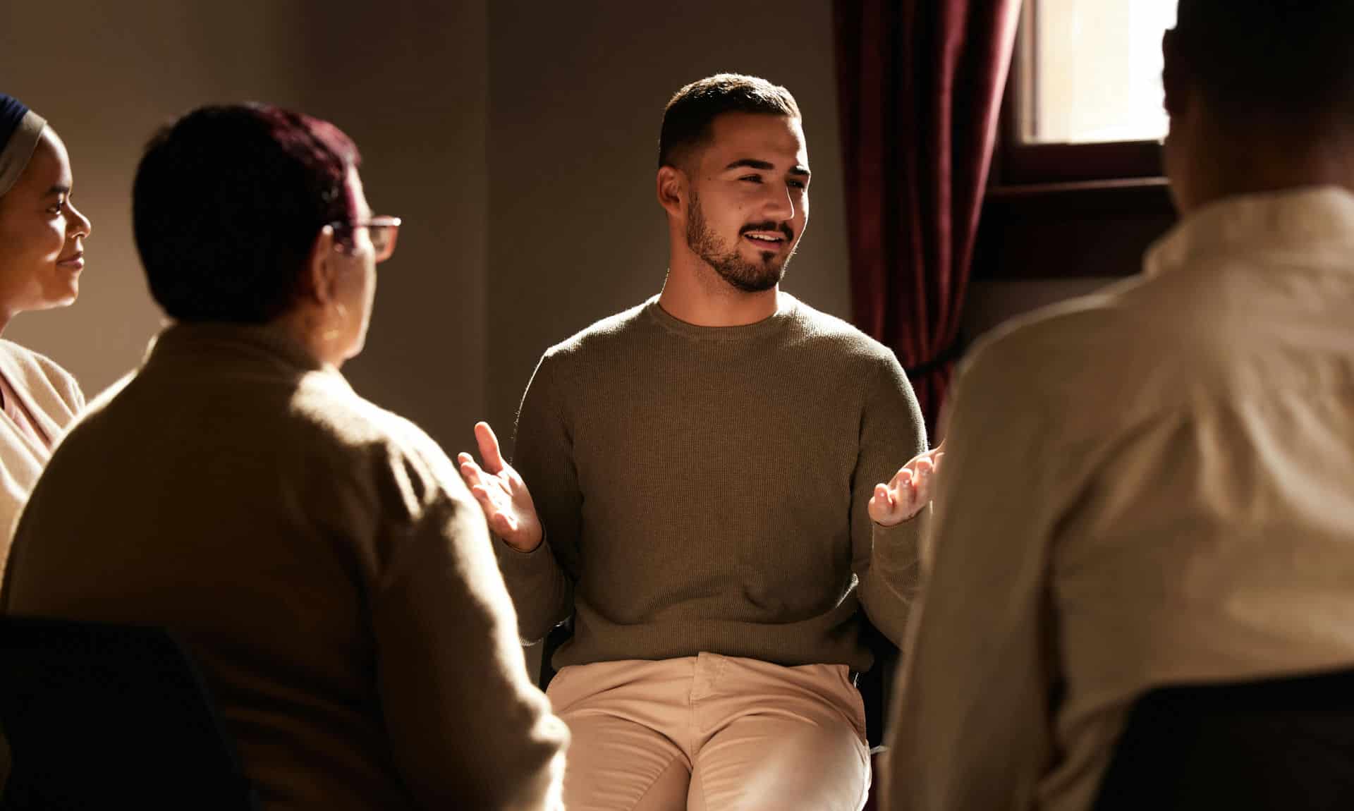 Man in shaded treatment room conversing with men and nonbinary people about binge eating disorder.