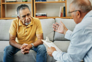 Older man having deep conversation with therapist with clipboard.