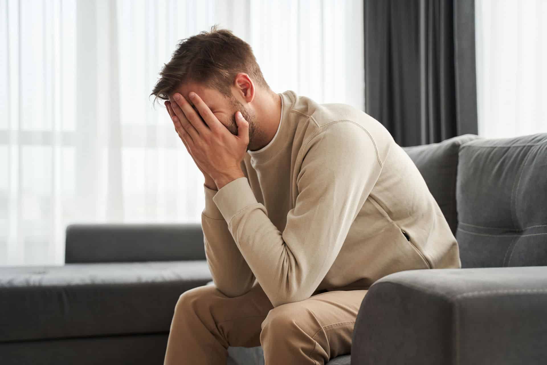 Man leaning forward and holding face in tiredness while sitting in couch.