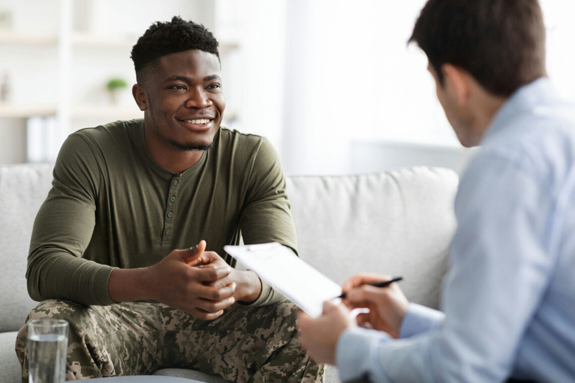 Man wearing military fatigues smiling while discussing caretaker burnout with therapist.